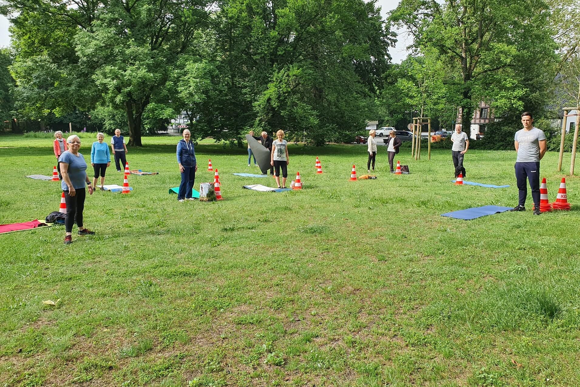 Gruppenübungen auf einer Wiese, Teilnehmer*innen stehen zwischen Conen und Yogamatten.