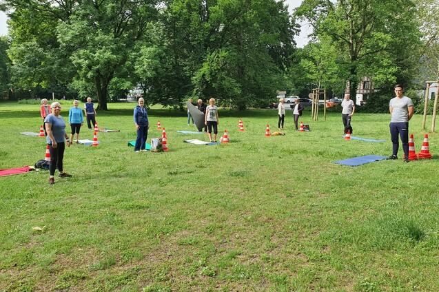Gruppen&uuml;bungen auf einer Wiese, Teilnehmer*innen stehen zwischen Conen und Yogamatten.
