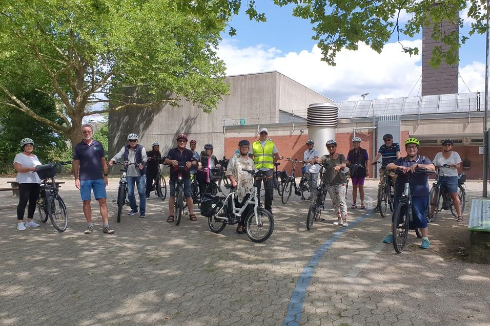 Gruppe von Radfahrern auf einem Platz, umgeben von B&auml;umen, bereit f&uuml;r eine Fahrradtour.