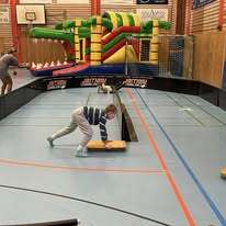 Kinder spielen in einer Sporthalle mit einem Kletterger&uuml;st und einer Rutschbahn auf einem gelenkten Parcours.