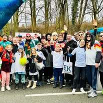 Gruppe von Menschen in Sporttrikots und Fanartikeln, die l&auml;chelnd f&uuml;r ein Foto posieren, im Freien unter B&auml;umen.