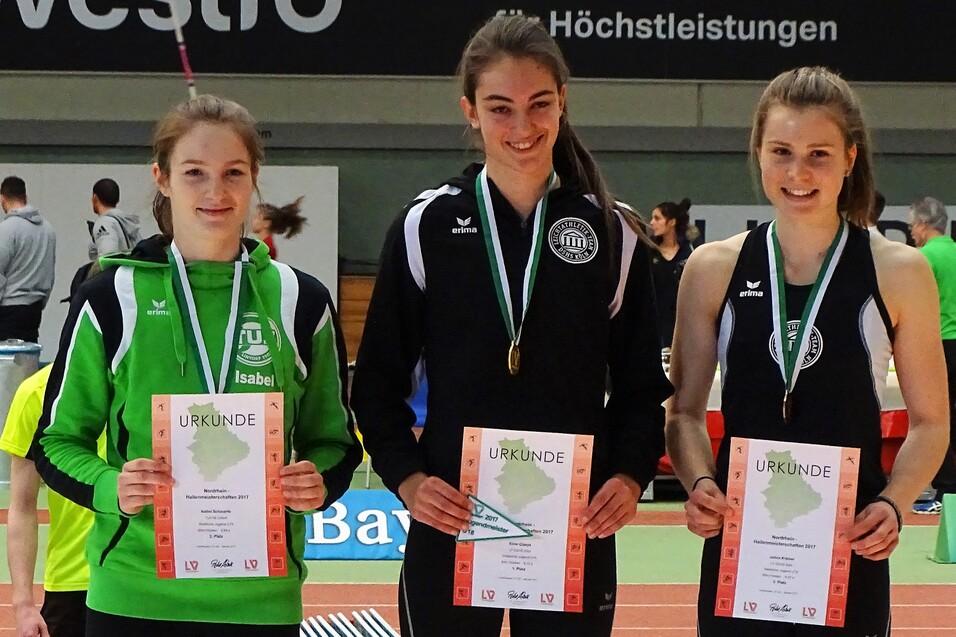 Drei junge Athletinnen mit Urkunden und Medaillen in Sportkleidung stehen l&auml;chelnd auf einem Wettkampfgel&auml;nde.