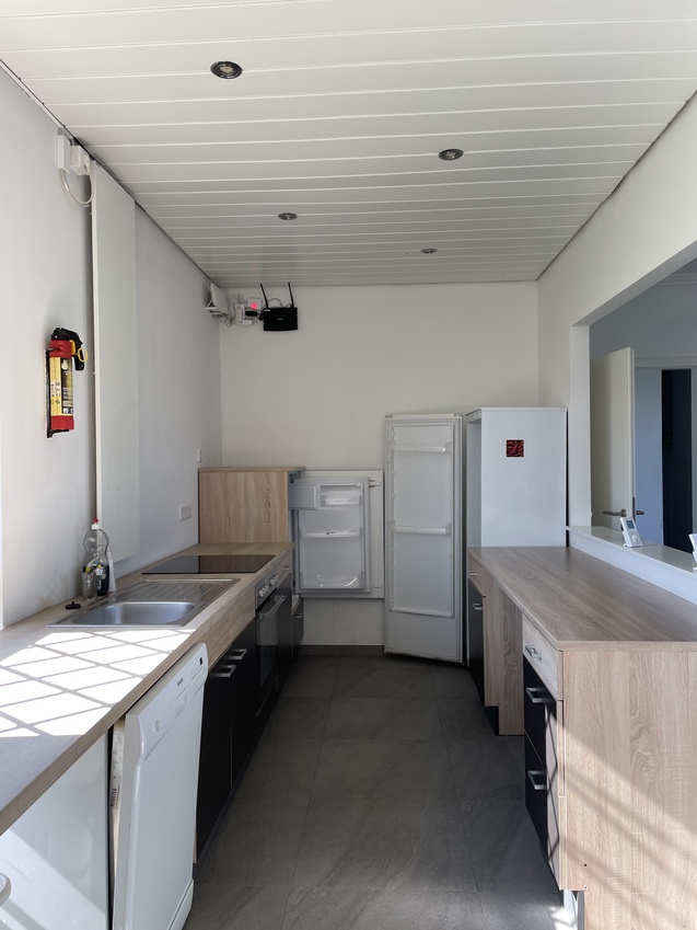 K&uuml;che mit Holzarbeitsplatte, Sp&uuml;le, Geschirrsp&uuml;ler und zwei K&uuml;hlschr&auml;nken an einer hellen Wand.