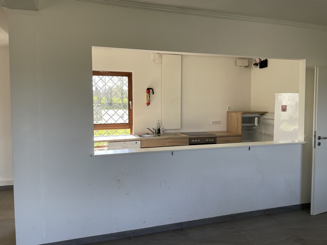 K&uuml;chenbereich mit einem offenen Durchgang, Holzarbeitsplatte und K&uuml;chenger&auml;ten in einem hellen Raum.