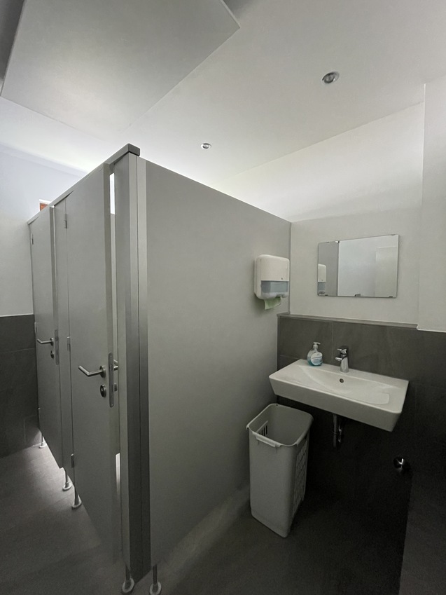 Innenansicht eines modernen Toilettenraums mit Trennw&auml;nden, Waschbecken und einem Spiegel an der Wand.