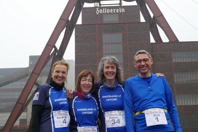 Vier L&auml;uferinnen und L&auml;ufer posieren vor dem Industriedenkmal Zollverein in einem st&auml;dtischen Umfeld.
