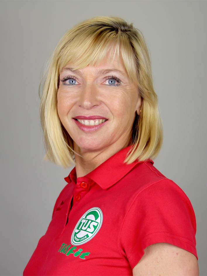 Porträt einer lächelnden Frau mit blonden Haaren in einem roten Poloshirt mit Logo. Hintergrund grau.