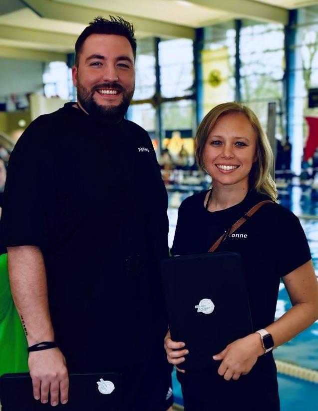 Zwei Personen stehen l&auml;chelnd am Schwimmbeckenrand und halten Tablets in den H&auml;nden.