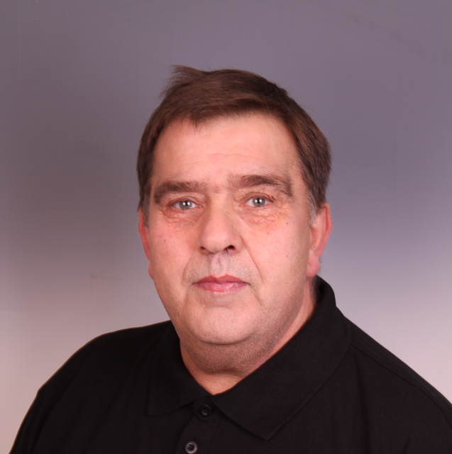 Portr&auml;t eines Mannes mit kurzen, braunen Haaren, der ein schwarzes Poloshirt tr&auml;gt und neutral in die Kamera blickt.